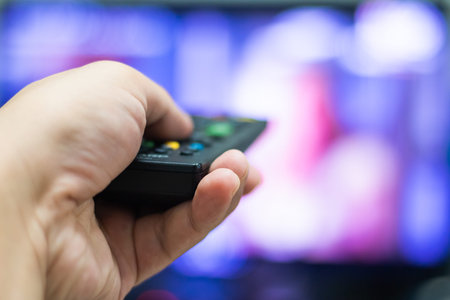 The man's hand presses the TV remote