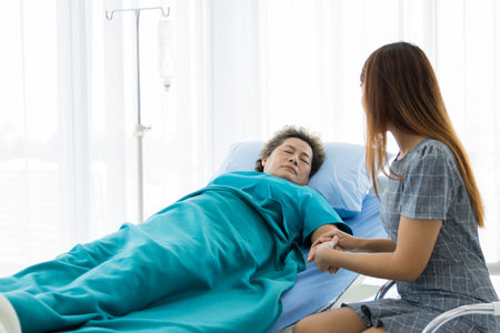 Asian families visit the elderly who are seriously ill at the hospital. A woman cared for the mother sleeping in the hospital with great concern. The concept of love of family, health insuranceの写真素材