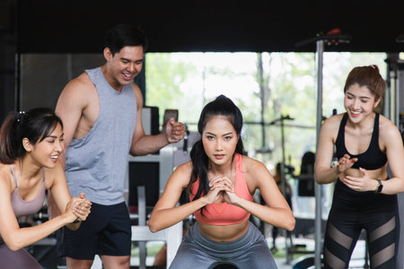 Portrait of a group of young asian fit people cheering on their friends Squats in fitness gym