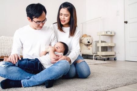 An Asian kid sucked a bottle of milk by lying on his father's lap and having a mother watch over his...