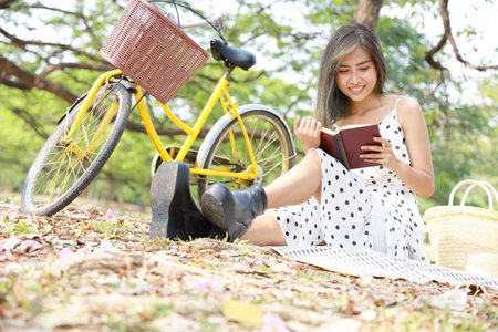 An Asian girl enjoying reading in the garden. A female office worker enjoying time away from technology. She turned off the phone and the computer. Visuals of digital detoxing conceptの写真素材