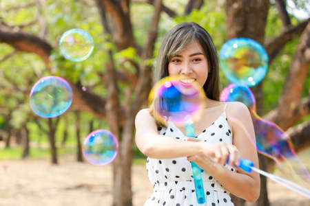 Outdoor autumn summer portrait of asian young beautiful happy woman making soap bubbles in park. Her Joyous happy in white dress. Holiday relaxation ideasの写真素材