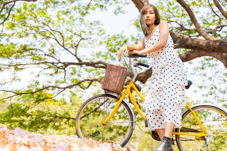 A beautiful Asian woman dressed in a vintage style. She led a yellow retro bicycle in the autumn park. Holiday relaxation ideasの写真素材