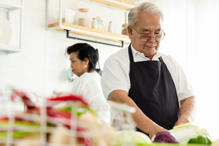 Portrait of an elderly Asian couple cooking in the home kitchen. They have a smiling face and are...