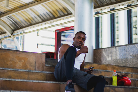 African men rest after exercising on the stairs with boxing gloves and energy drinks.