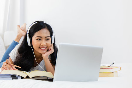An Asian woman Education online from home. She student looking at laptop listening lecture study...