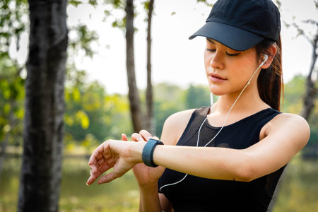 an asian women runner using smart watch to monitor her performance. athlete setting fitness app on...