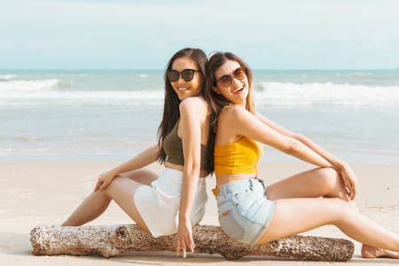 Two Asian women friends in summer casual clothes Take a photo together at the beach on vacation in tropical country. Young beautiful Female joy in the beach on a sunny dayの写真素材