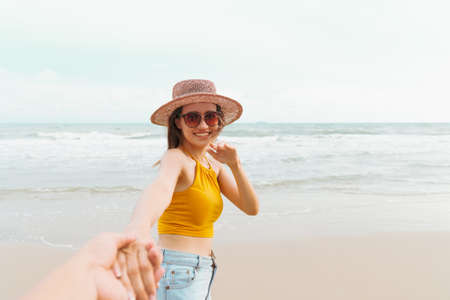 Asian Woman holding boyfriend hand and running on tropical beach to the sea on a holiday. An excited woman run and pulls her man hand to the beach on a summer day. Follow me.の写真素材