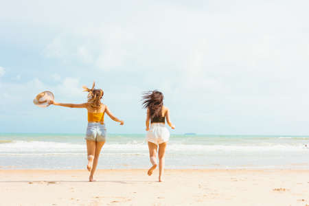 Two Young Asian woman on vacation walking and enjoy the seaside. Female friends wearing sunglasses, smiling having fun on vacation in tropical beach. Travel on summer day conceptの写真素材