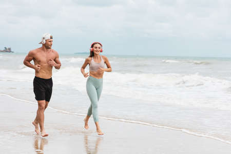 A caucasian man and woman runner in sportswear Outdoor jogging at the beach. Young fitness sport couple wearing headphones running at seaside. healthy exercise conceptの写真素材