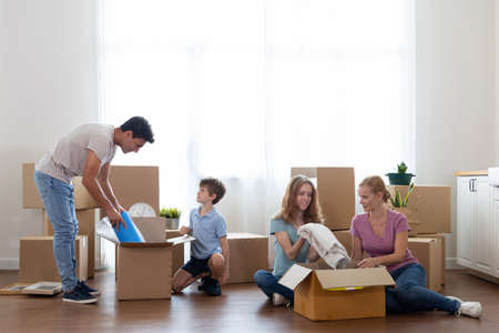 Caucasian family pick up waste items and clothes and put them in a paper box to donate and reuse or recycle. Parents and children  pick up item in boxes for moving into the new homeの写真素材