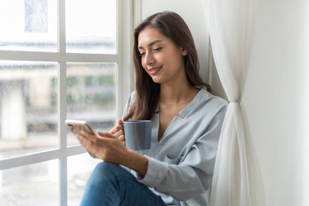 Pretty young caucasian woman sitting sofa enjoying first morning coffee on sunshine and use...