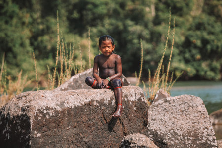 Indian boy from tribe in the Amazon, sitiing on a rock by the Xingu River in Brazil, 2010.のeditorial素材