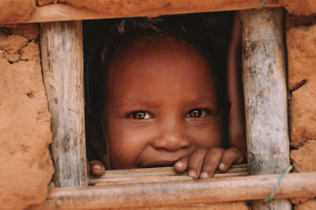 Poverty-stricken child looking and smiling through the small window of a mud house in the North of Brazil.のeditorial素材