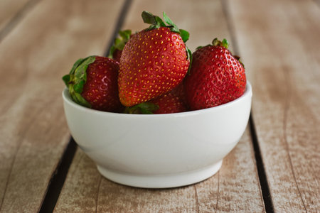 Strawberries in a white bowl supported on brown board tableの写真素材