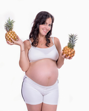 A pregnant woman with to pineapple in her hands wearing white clothes.の写真素材