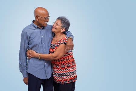 Elderly couple standing, hugging and looking at each other. Light blue gradient backgroundの写真素材