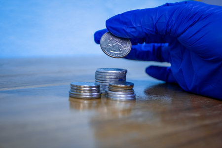 Protected hand with a blue glove manipulating money coins