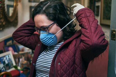 Girl preparing to leave home wearing disposable gloves and a mask for protection against coronavirusの写真素材