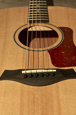 Detail of the bridge and sound hole of an acoustic guitar with red pick guard on a brown wooden...