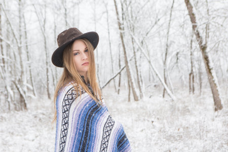 young woman in the snow wearing a bohemian style blanket and hat during a winter storm.