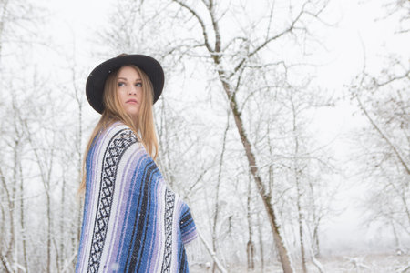 young woman in the snow wearing a bohemian style blanket and hat during a winter storm.