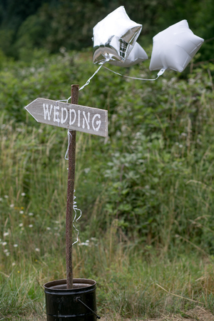 Old rustic looking hand painted wedding sign that is pointing in a direction toward a wedding with star ballons in an rural setting.の写真素材