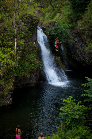 June 28, 2018 , Muai Hawaii - A man leaps into a deep pool next to a waterfall in a stream in Hawaii with on lookers watching.のeditorial素材