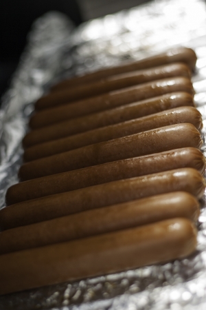 Row of tasty brown sausages being grilled on tinfoil with shallow dofの写真素材