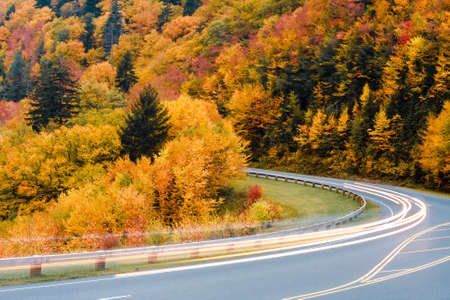 Blurred car lights on a mountain road against a colorful Autumn scene.の写真素材