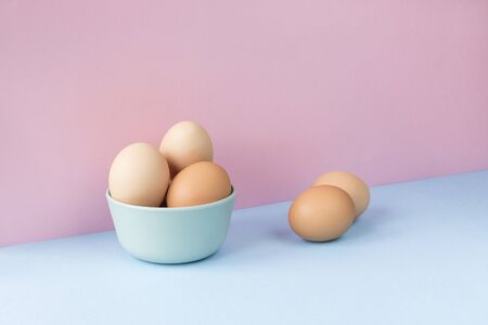 Minimalist image of several brown eggs in a bowl on a light blue and pink background. Copy space available.の写真素材