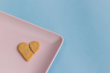 Broken heart. Heart shaped cookie isolated on a pink tray. Light blue background. Copy spaceの写真素材