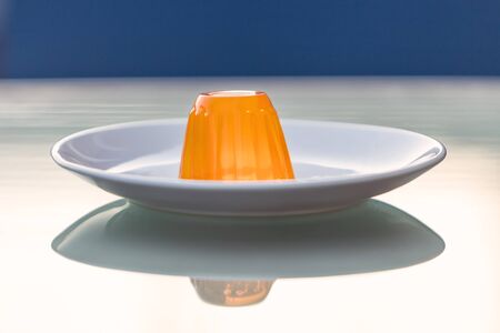 Close-up of an orange gelatin on a white plate reflected on a glass tableの写真素材