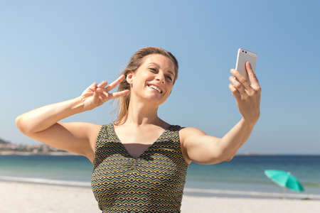 Close-up of a middle-aged blonde woman in a green dress making a selfie on the beach with the sea in the backgroundの写真素材