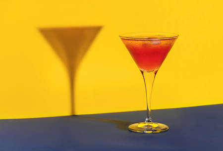 Red cocktail in a glass shaping its shadow on a blue and yellow backgroundの写真素材