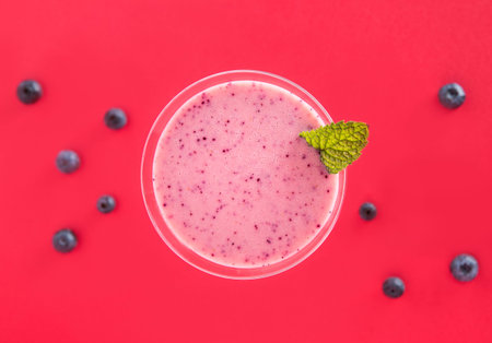 Blueberry smoothie cup with several blueberries on a red background.Top view.