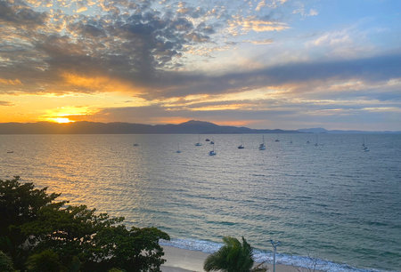 Sunset at Praia de Jurere, with blue and orange sky, showing the beach, clouds in the sky, mountains in the background and fishing boats in the sea.の写真素材