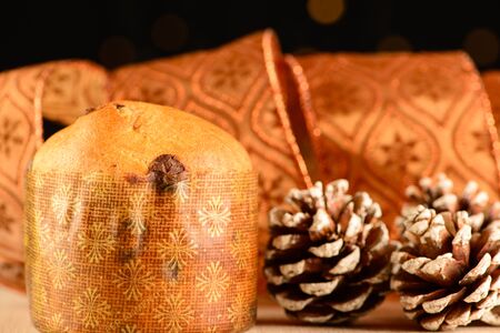 small panettone next to pine cones and decorative ribbon with dark background and small lightsの写真素材