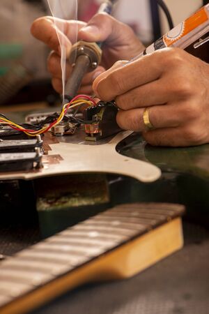 luthier soldering a guitar wire in his workshopの写真素材