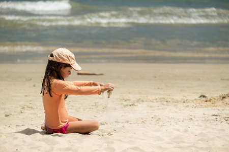 little girl playing alone sitting on the beach sand.の写真素材