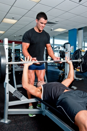 Fit young man lifting weights in a gym assisted by a personal trainer in a health and fitness conceptのeditorial素材