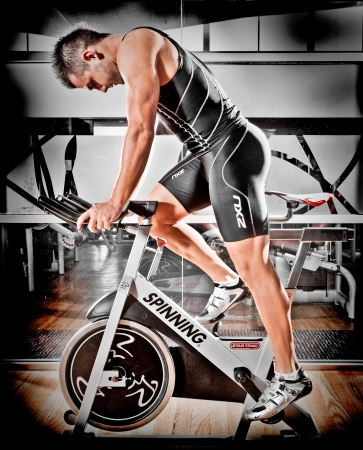 Strong fit athletic man training in a gym on a spinning bike in a health and fitness concept, sideways profileのeditorial素材