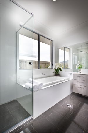 Modern minimalist bathroom interior with a glass shower cubicle and bath tub under a window in shades of grey and whiteのeditorial素材