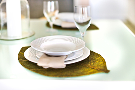 Closeup of an empty dish on green leaf shaped decoration like braid, There are wine glasses near the it. The background is blurred. There are three dishes one on another.の写真素材