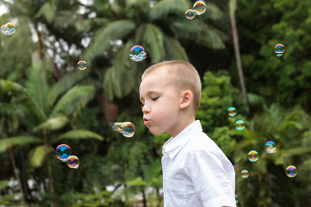 a beautifull picture of kid playing with bubbles in t he garden wearing white t-shirt, background is...