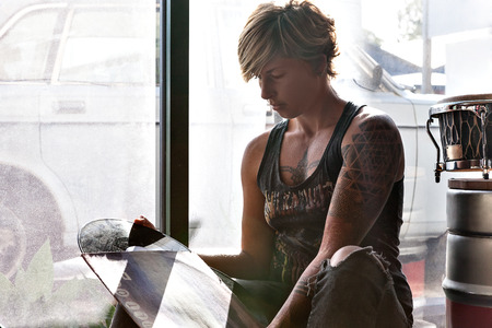 Tattoo girl with gold color short hair takes out the vinyl disk from the album cover and sitting beside a glass windowの写真素材
