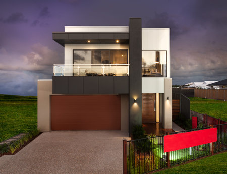 Luxury house with a green grass lawn with a fence around and the sky is dark and purple, there is a garage and a concrete floor in front of it.の写真素材