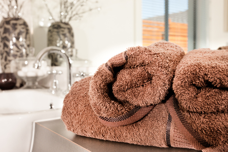 Towel has fur and very thick from the view, it is a dark brown color textile in a modern washroom, there is a sink with a faucet and some fancy items blurred in the backgroundの写真素材