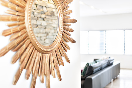 Round mirror on the wall with wooden pieces attached to it with some carve close up in a blurred living room with the sunlight illuminationの写真素材